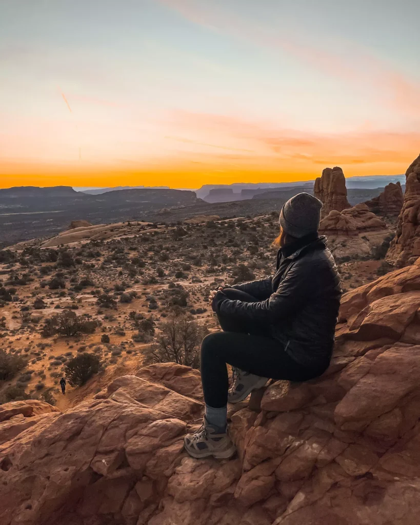 Girl sitting on rock looking out over sunrise in arches national park
