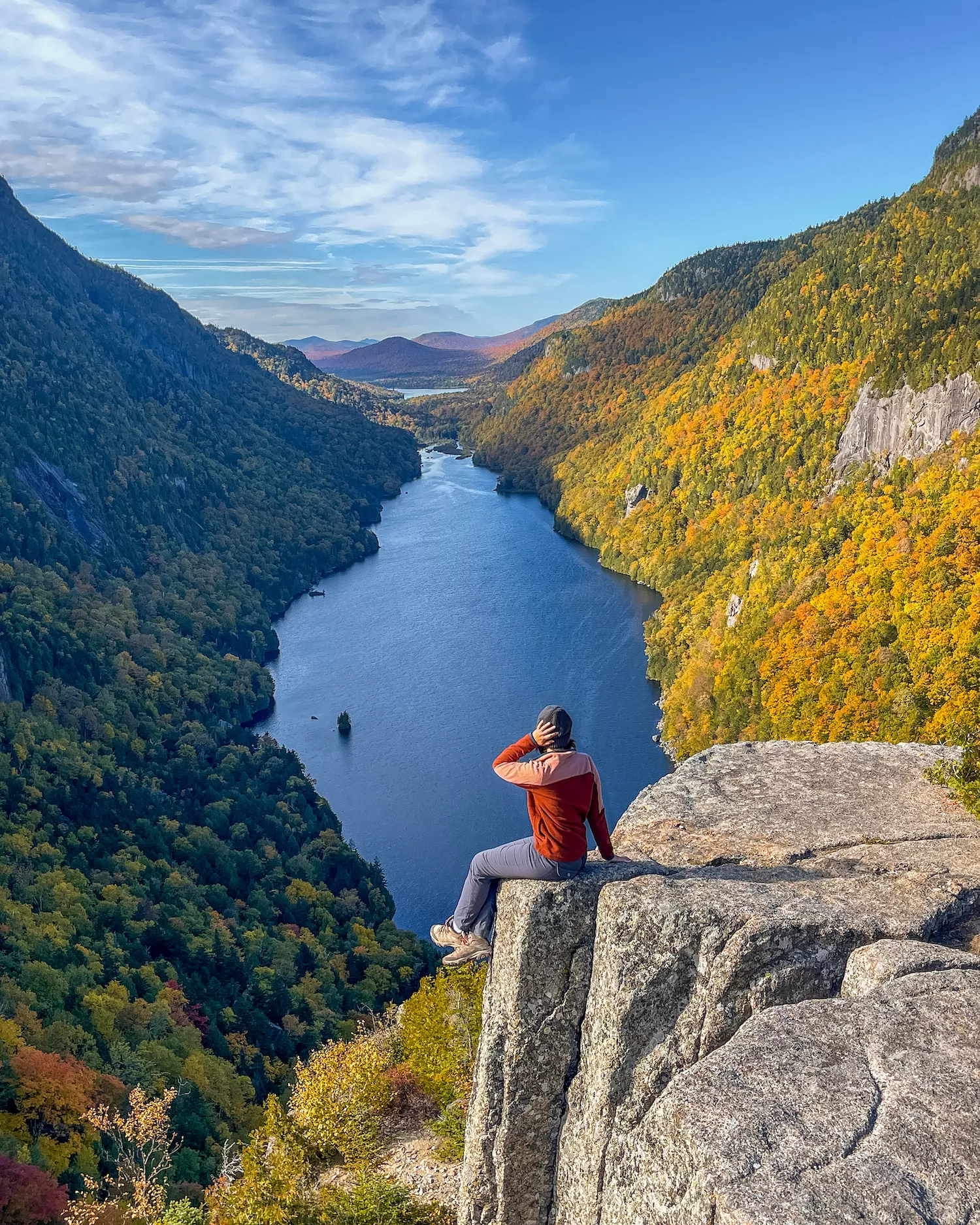 girl sitting on top of Indian Head mountain with lake below her and fall colored trees around her
